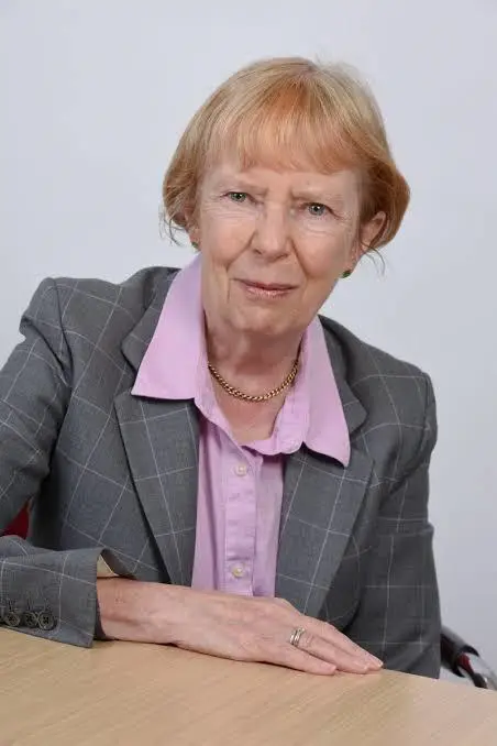 A woman with short light coloured hair wearing a shirt and blazer smiling at the camera
