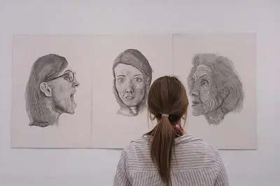 Visitor views three large pencil portraits displayed on a white gallery wall.