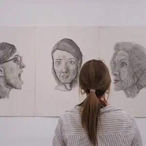 Visitor views three large pencil portraits displayed on a white gallery wall.