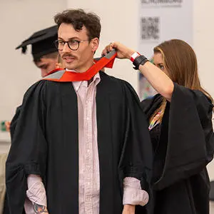 A student being dressed in a graduation gown