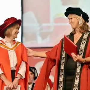Two women in red academic robes talk to each other during a graduation ceremony.