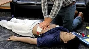 Instructor performs chest compressions on a training mannequin during a CPR demonstration.