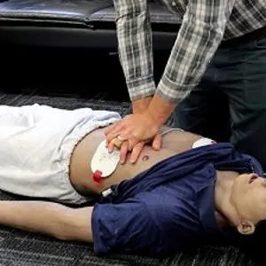 Instructor performs chest compressions on a training mannequin during a CPR demonstration.