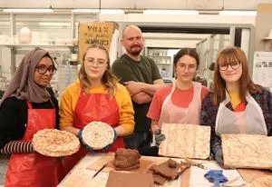 School pupils and a tutor display handmade ceramic pieces and textured tiles in a workshop.