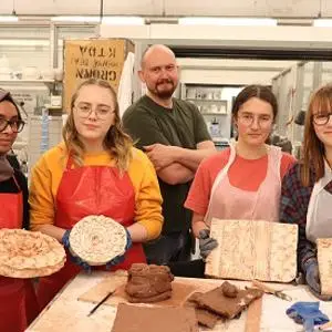 School pupils and a tutor display handmade ceramic pieces and textured tiles in a workshop.