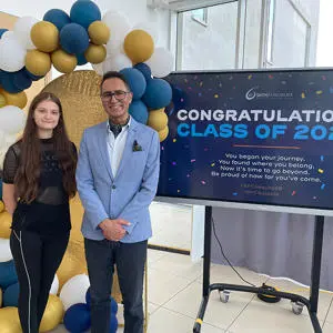 A female student and man smiling in front of a balloon arch