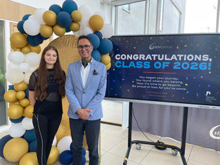 A female student and man smiling in front of a balloon arch