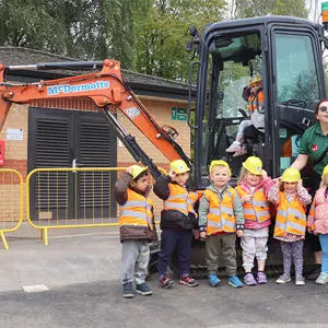 A group of children in hard hats standing in front of a digger