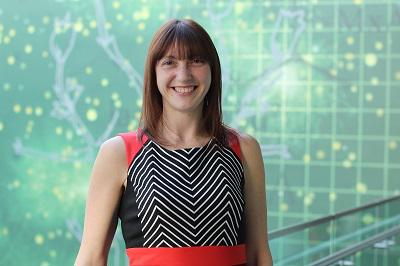 Smiling woman in a black patterned dress stands before a green digital network graphic.