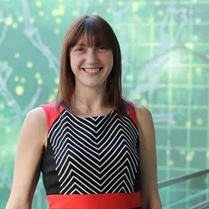 Smiling woman in a black patterned dress stands before a green digital network graphic.