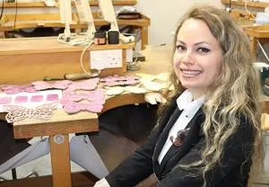 Smiling woman sits at a workshop bench covered with pink butterfly-shaped designs.