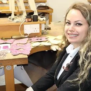 Smiling woman sits at a workshop bench covered with pink butterfly-shaped designs.
