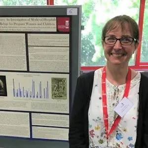 Smiling woman stands beside a detailed academic research poster at a conference.