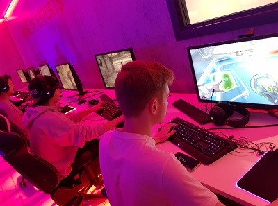 Student plays at a desktop computer in a purple-lit esports room.