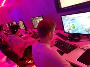 Student plays at a desktop computer in a purple-lit esports room.