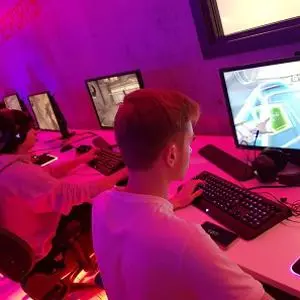 Student plays at a desktop computer in a purple-lit esports room.