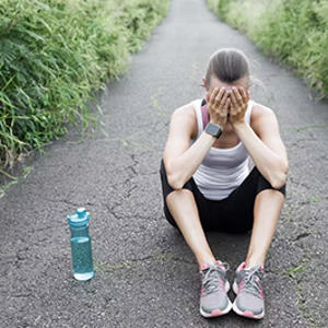 A runner pictured sitting on the ground next to a water bottle with their head in their hands