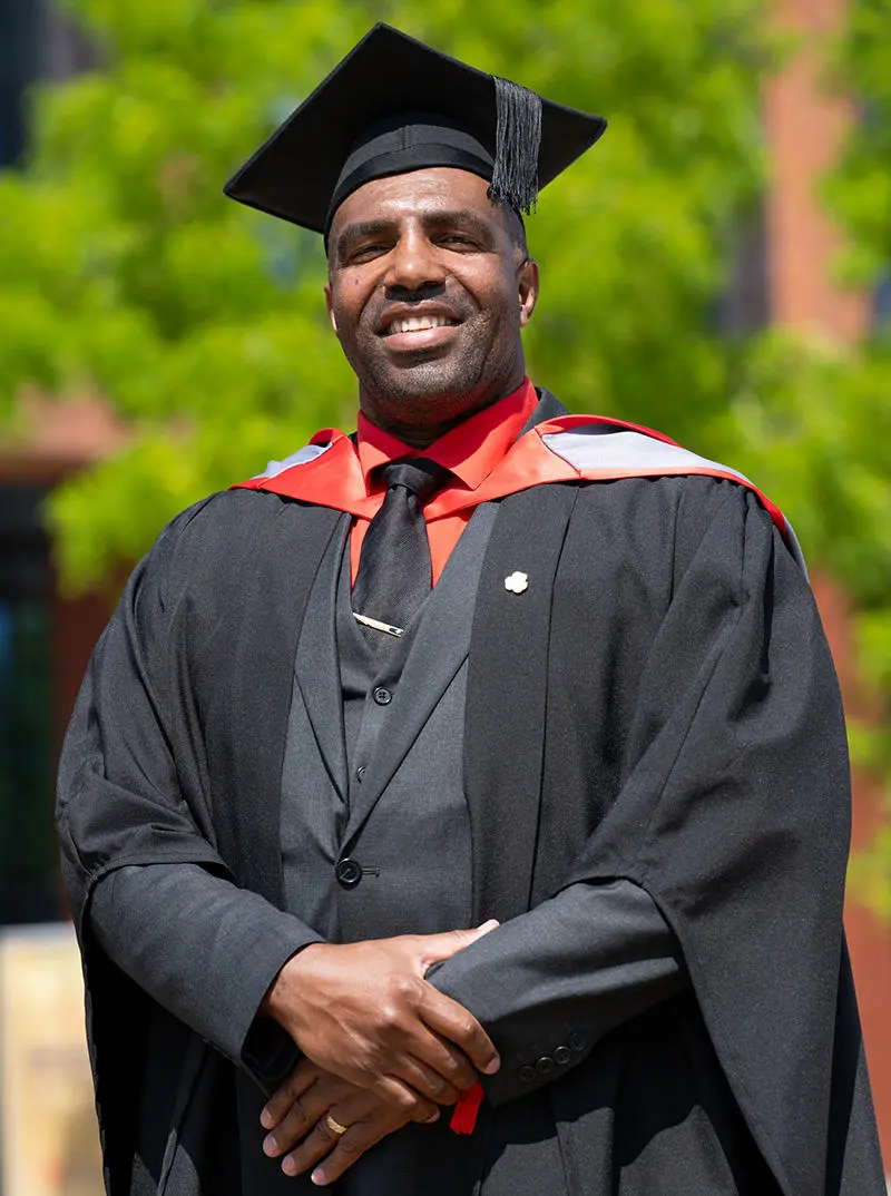 A smiling man wearing a graduation cap and gown