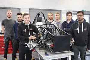 Formula Student team poses around the exposed frame of a single-seat racing car.