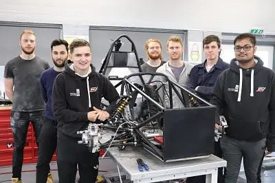 Formula Student team poses around the exposed frame of a single-seat racing car.