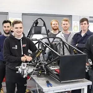 Formula Student team poses around the exposed frame of a single-seat racing car.
