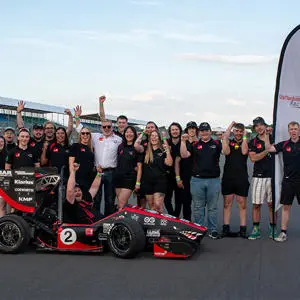 A group of Staffordshire University students on Silverstone racing track with the racing car they designed