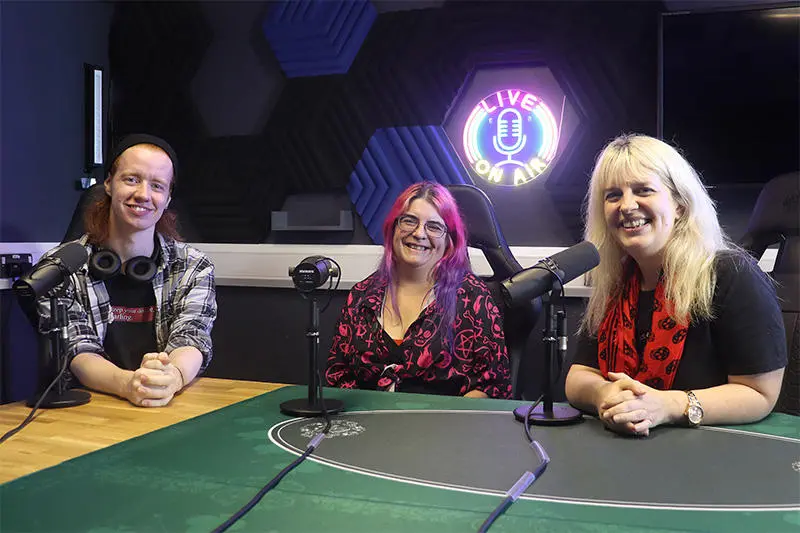 Three people sat in a podcast recording studio
