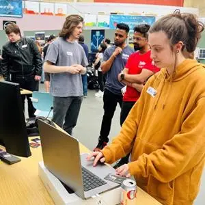 Girl on laptop computer and men stood around conversing