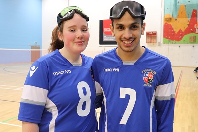 Two goalball players in blue numbered jerseys pose with protective goggles on their heads.