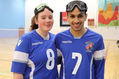Two goalball players in blue numbered jerseys pose with protective goggles on their heads.