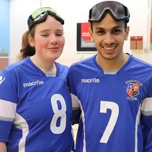 Two goalball players in blue numbered jerseys pose with protective goggles on their heads.