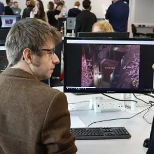 Man and woman discuss game graphics displayed on computers in a busy digital lab.