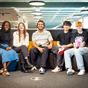 Five smiling students sat together on a sofa