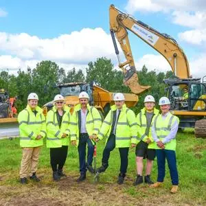 Six people in high vis and hardhats in field with heavy machinery