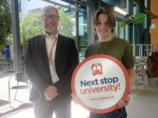 A man stood next to a teenage boy holding a sign saying 'next stop university!'