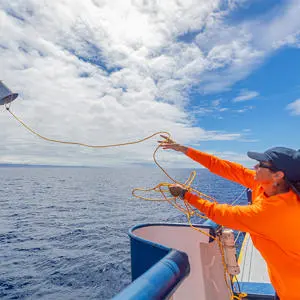 A person in an orange jumper throwing a bucket from a boat