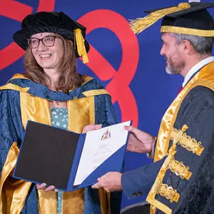 Heather McLachlanin wearing her honorary doctor cap and gown receiving her award from Major Levison Wood