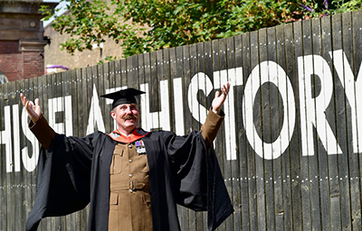 A member of the armed forces pictured in uniform and a graduation gown