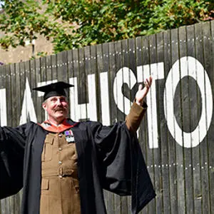 A member of the armed forces pictured in uniform and a graduation gown