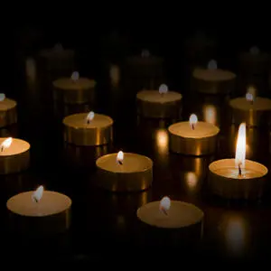 Rows of small memorial candles glow against a black background.