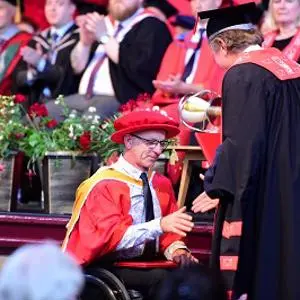 Man in red cap and gown being congratulated at formal ceremony