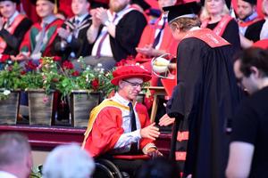 Man in red cap and gown being congratulated at formal ceremony