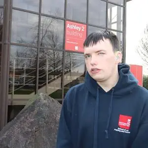 Young man in a dark university hoodie stands outside the Ashley 2 building.
