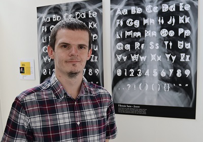 Man stands in front of posters displaying hand-drawn alphabet and symbol designs.