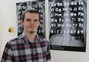 Man stands in front of posters displaying hand-drawn alphabet and symbol designs.