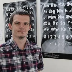 Man stands in front of posters displaying hand-drawn alphabet and symbol designs.