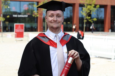 James Grist in his graduation robes holding a scroll