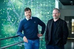 Two men stand together in front of a green digital network graphic.