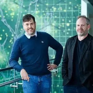 Two men stand together in front of a green digital network graphic.