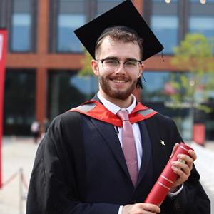 Jared Darcy in his graduation robes holding a scroll
